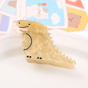 Close-up of a marble-textured yellow dinosaur acrylic hair claw clip on a ceramic tray