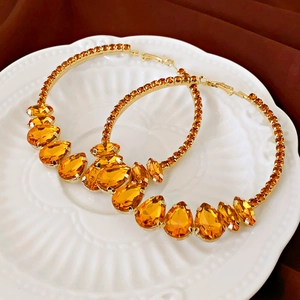 Detailed shot of gold hoop earrings with amber pear-cut stones on a white relief plate