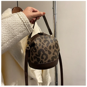 Detailed view of spherical crossbody bag with leopard print and brown leather handles