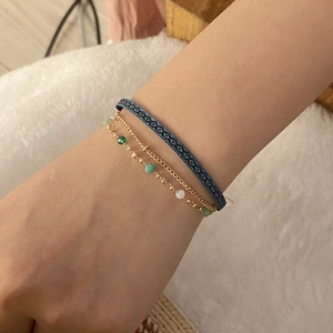 Detail of layered bohemian bracelets with blue woven rope and golden beaded chains
