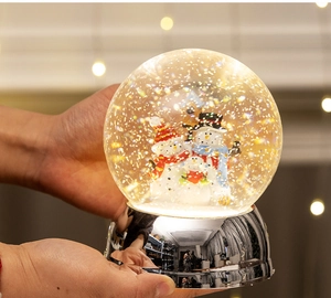 Close-up of glowing Christmas snow globe with snowman family and silver mirror base