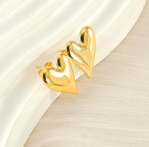 Macro detail of polished 18K gold plated heart stud earrings on textured surface