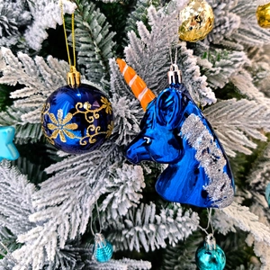 Boule de Noël bleue à motifs dorés et ornement licorne sur une branche enneigée