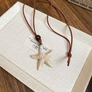 Detail of a beige starfish pendant on a dark brown leather cord with a wooden bead