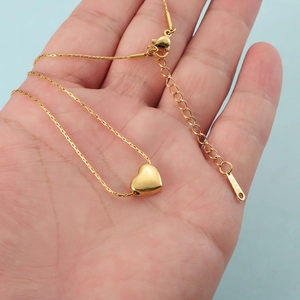Minimalist gold heart pendant necklace in stainless steel shown on hand for scale