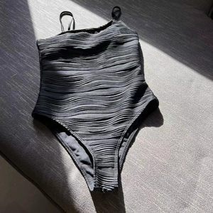 Detail of black one-piece swimsuit featuring unique wavy textured fabric and thin straps