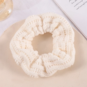 Detailed close-up of a beige knitted hair scrunchie with soft woven fabric texture