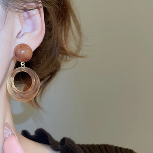 Close-up of amber resin drop earrings with hollow round pendants on a female model