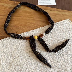 Close-up of leopard print fabric necklace featuring resin and wooden beads on a white fringe rug
