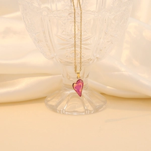 Golden cross chain necklace with a translucent pink heart crystal pendant on silk fabric