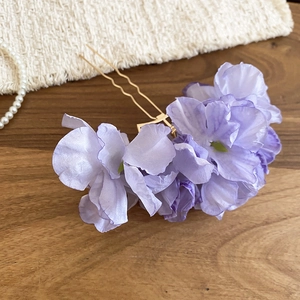 Detail of purple fabric flower hair pin with gold U-shaped fork on a wooden background
