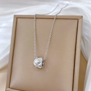 Macro detail of silver cylinder pendant with diamond cut pattern on minimalist necklace