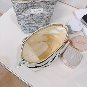 Detail view of striped canvas and tweed cosmetic bags with makeup accessories on white desk
