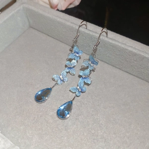 Macro detail of blue butterfly drop earrings with shimmering crystal tassels and silver hooks