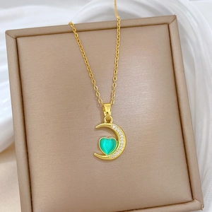 Close-up of golden crescent moon pendant with green heart gem and micro-pave crystals