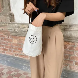 Detail of white canvas bucket bag with black smiley face and leather handle