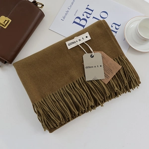 Detail of soft brown cashmere scarf with fringe edges and brand label on a cozy table