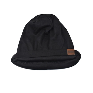 Detail of a black knitted beanie featuring a brown leather 'FASHION' label on the side