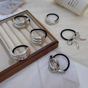Macro detail of silver metal bow and textured curved hair ties on cream velvet display