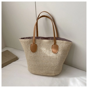 Detail view of woven straw tote bag with brown handles on a white soft surface