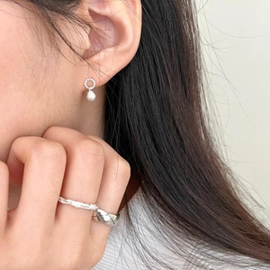 Close-up of elegant pearl drop earrings and silver twist rings worn by a model