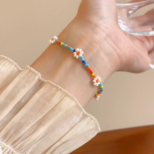 Close-up of rainbow seed bead bracelet with white flower charms on a woman's wrist