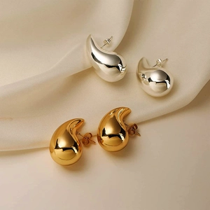 Polished gold and silver teardrop earrings on elegant beige silk fabric texture