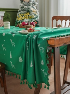 Detail of green Christmas tablecloth featuring white reindeer, tree patterns and fringe