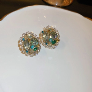 Macro shot of gold earrings with green gemstones and turquoise beads on a white tray