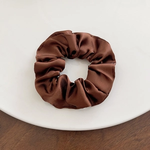 Detail of a dark brown satin scrunchie with silky texture on a white round tray