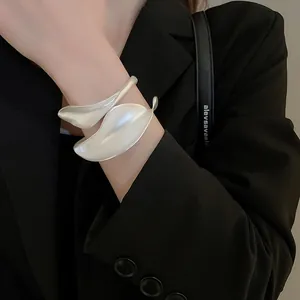 Detail of matte silver leaf-shaped open cuff bracelet worn by a model in a minimal style