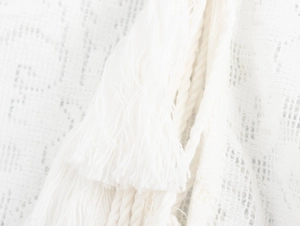 Close-up of intricate lace fabric with white tassels and bohemian mesh texture