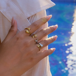 Close-up of gold and silver sun and moon star rings worn against a sparkling blue pool water