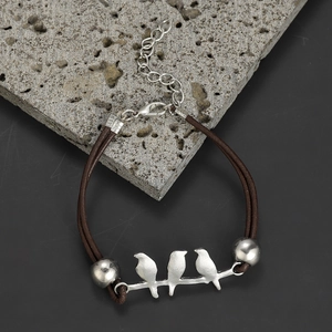 Detailed view of hummingbird metal charm on a dark brown leather bracelet with silver clasp