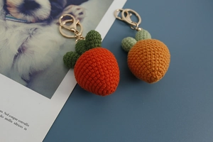 Macro shot of two handmade crochet carrot and strawberry pendants with keyrings