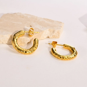 Detailed view of gold C-shaped earrings with unique hammered metal texture on stone