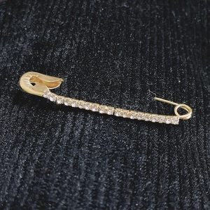 Vue macro d'une épingle de taille dorée avec strass brillants sur tissu texturé sombre