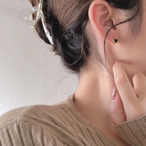 Close-up of heart-shaped black enamel stud earring with gold-plated trim on model