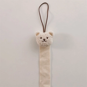 Detail of beige plush bear pendant with herringbone ribbon and brown leather loop