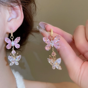 Detail showing gold butterfly earrings with pink and white cubic zirconia on a model