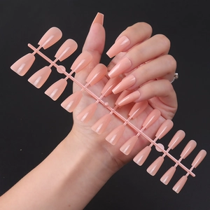 Detailed view of glossy nude coffin-shaped press-on nails set on a dark grey background