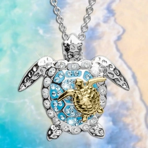 Close-up of double turtle necklace with blue crystals and gold accents on a beach backdrop