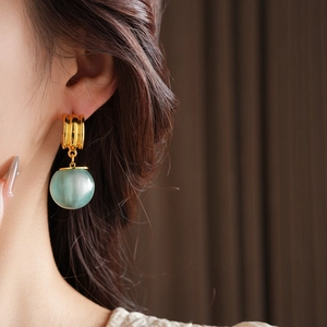 Detail of light green resin ball earrings with gold-tone studs worn by a model