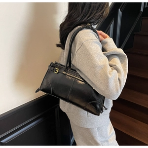 Detail of black leather shoulder bag with gold buckle and adjustable strap on a model