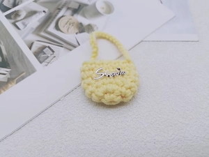 Dettaglio della mini borsa gialla all'uncinetto con logo in metallo su sfondo bianco