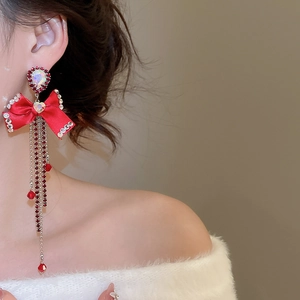 Macro shot of red ribbon bow earrings with cascading rhinestone tassels on a model