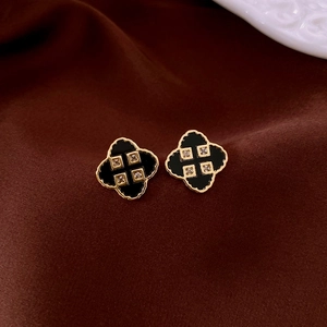 Detailed close-up of gold clover stud earrings with black enamel on silk fabric background
