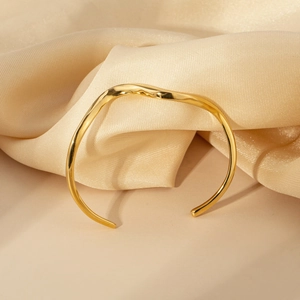 Polished 18K gold S-shaped wavy open bangle with minimalist aesthetic on champagne silk