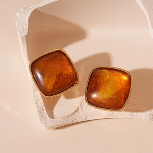Detailed close-up of amber resin square stud earrings with gold trim on stone decor