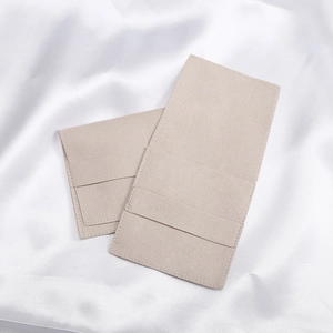 Macro view of beige microfiber jewelry pouches with flap design on white satin fabric